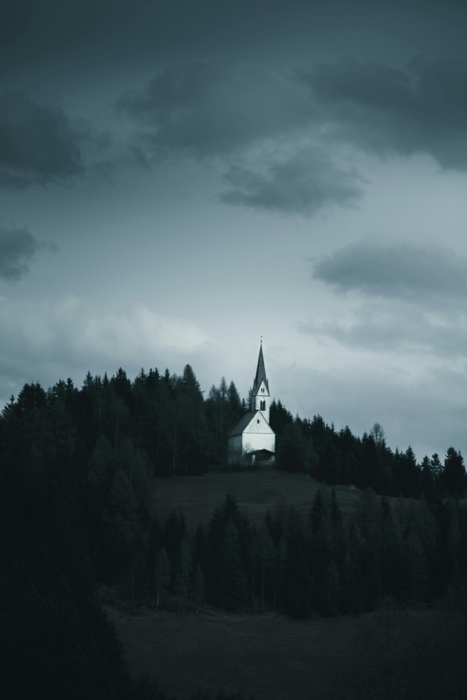 Eerie landscape of a lone church on a misty hill under dramatic clouds, evoking mystery.